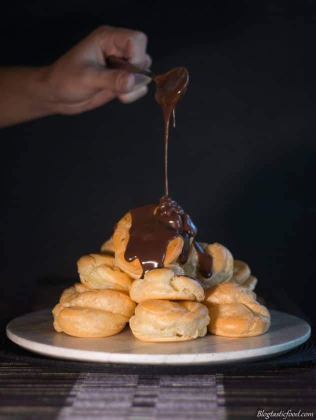 Melted chocolate being drizzled over a stack of profiteroles.