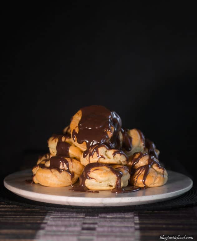 A stack of profiteroles with melted chocolate on top.