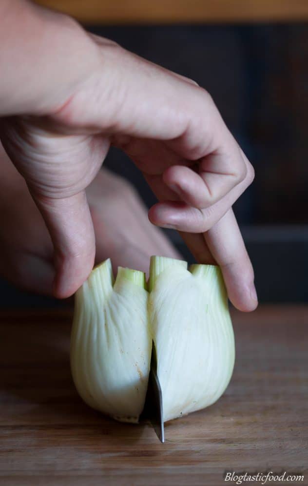 Some using a knife to cut a bulb of fennel in half. 