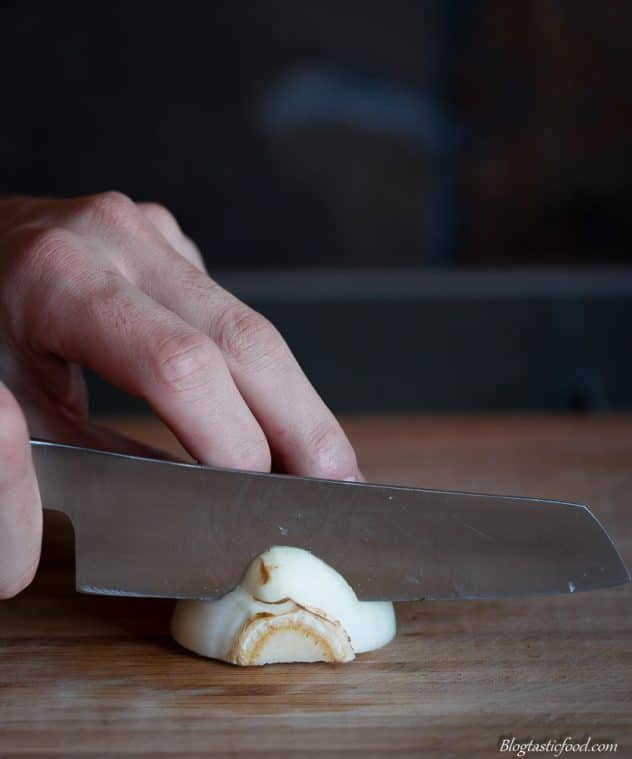 Someone cutting the bottom root part of a fennel bulb with a knife. 