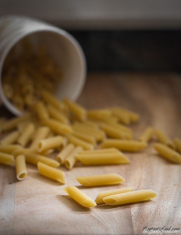 Dried penne pasta on a board with a mug in the background. 
