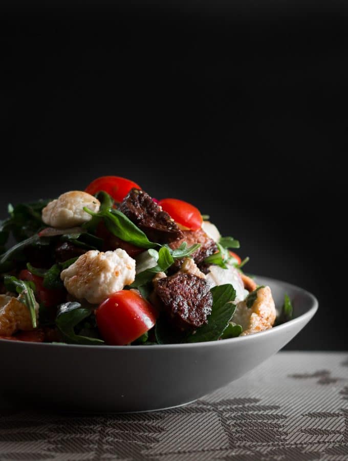 A dark, moody contrast photo of crispy chorizo and fried halloumi salad.