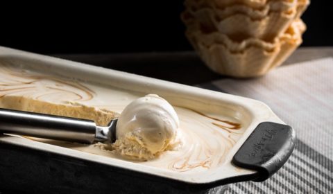 Baileys and salted caramel ice-cream being scooped out of a tin with waffle cups in the background.