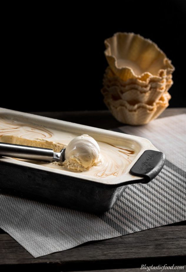 Baileys and salted caramel swirl ice-cream being scooped out of a loaf tin with waffle cups in the background. 