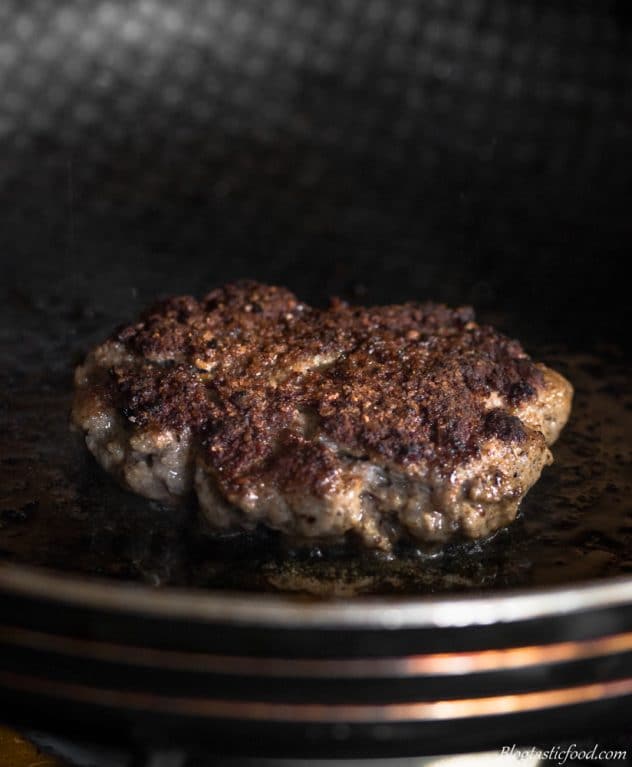 A beef patty frying off in a non-stick frying pan. 