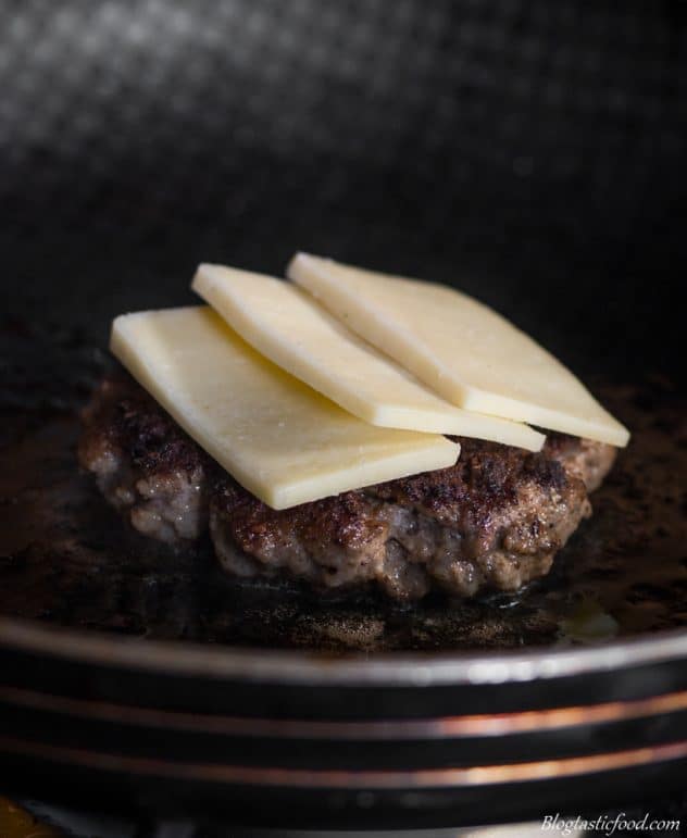 A burger patty frying in a pan with 3 slices of cheese on top of it. 