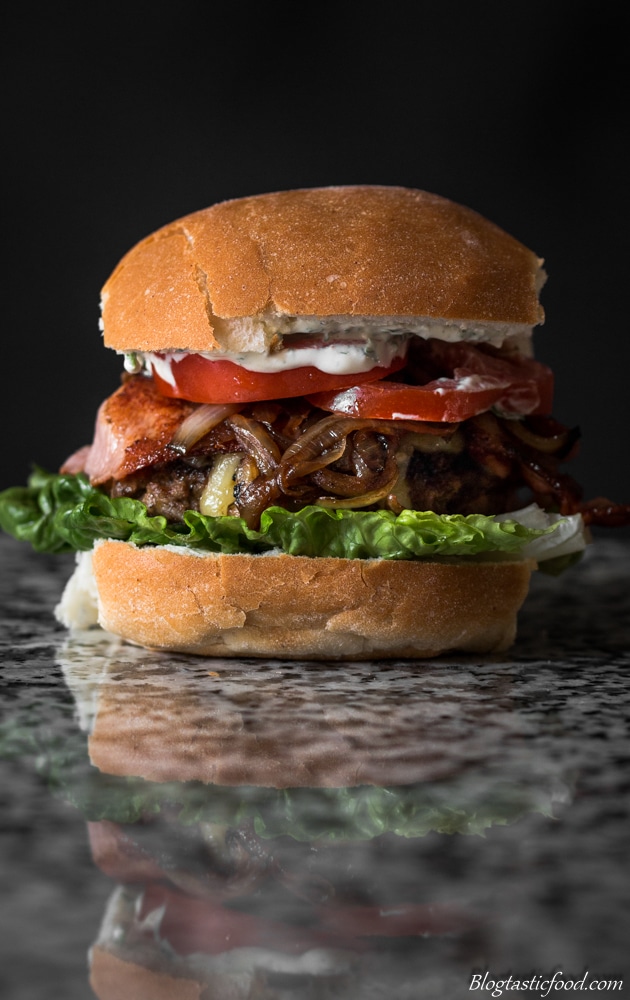 A eye level photo of a beef and bacon burger on a granite surface.  