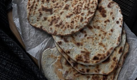 A photo of flat breads served on top of a chopping board and scrunched up baking paper.
