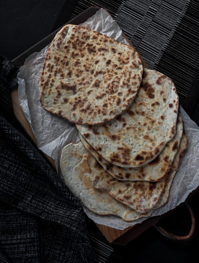A photo of flat breads served on top of a chopping board and scrunched up baking paper.