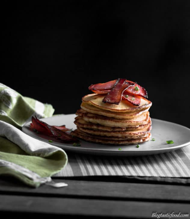 A stack of thick, fluffy pancakes topped with crispy bacon coated in maple syrup.