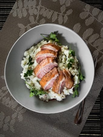 Slices of medium rare pan seared duck breast on herb risotto.