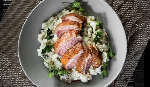 Slices of medium rare pan seared duck breast on herb risotto.