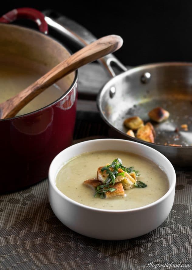 Roasted cauliflower and leek soup served in a bowl that has been garnished with croutons and basil. 
