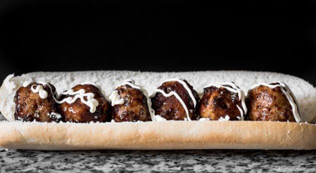 An eye level photo of a bread roll filled with meatballs and Japanese mayo. 