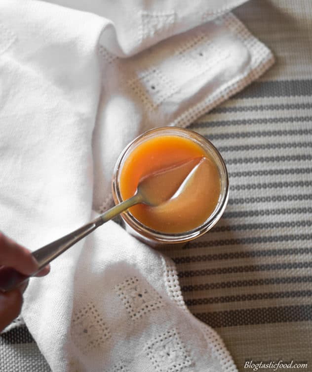 A spoon going into a jar of salted caramel.