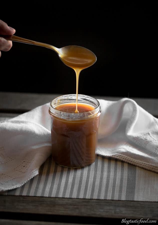 A spoon drizzling salted caramel into a jam jar.