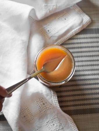 An overhead shot of a silver spoon going into a jar of salted caramel sauce.