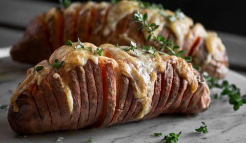 A photo of cheesy Hasselback sweet potatoes on a marble surface.