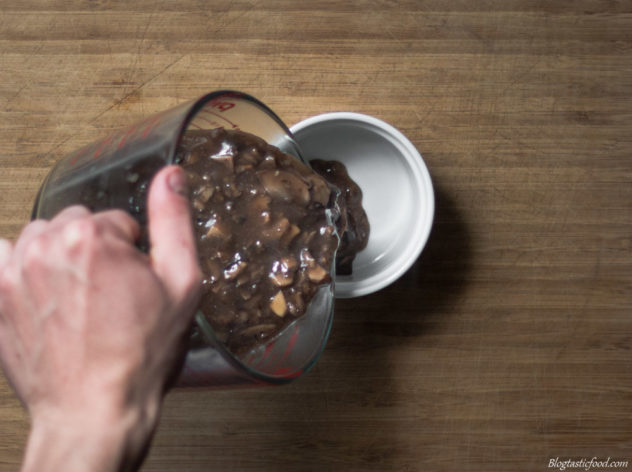 A photo of mushroom gravy getting poured into a ramekin.