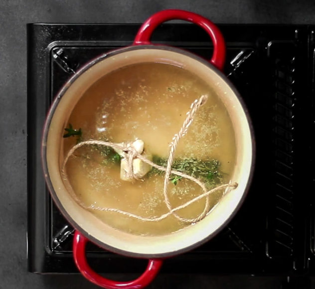 A photo of a bouquet garni inisde a pot of simmering stock.