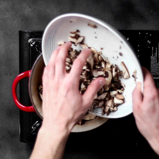 A photo of mushrooms being added to a pot.