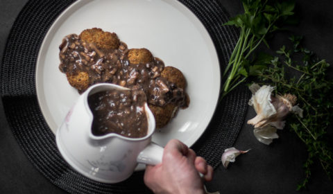 mushroom gravy being poured over 3 breaded fillets of fish.