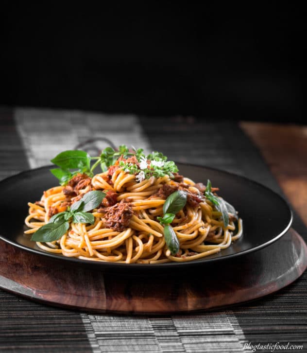 A photo of shredded beef spaghetti bolognese on a black plate.