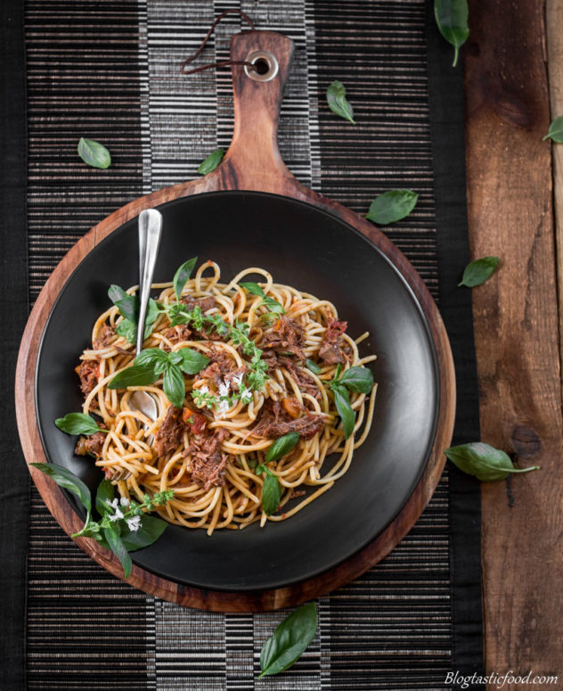 An overhead photo of shredded beef spaghetti bolognese garnished with basil.