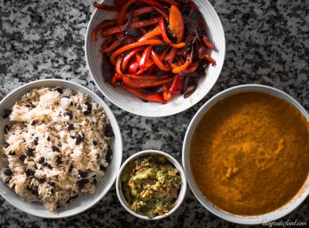 An overhead photo of black beans and rice, sauteed red onions and peppers, salsa and guacamole in separate bowls. 