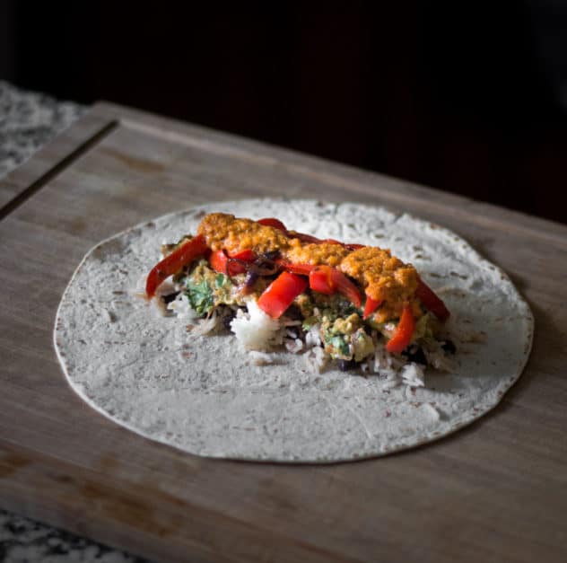 A photo of all guacamole, salsa, rice, beans, red peppers and red onions in the middle of a tortilla. 