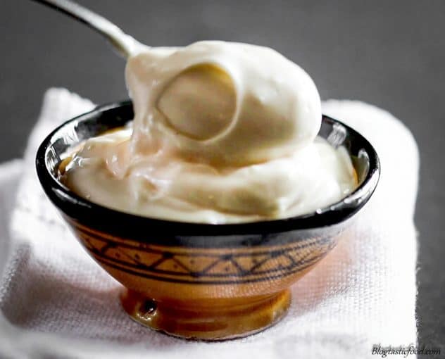 A close up photo of light, creamy mayo in a bowl with a spoon lifting it up.