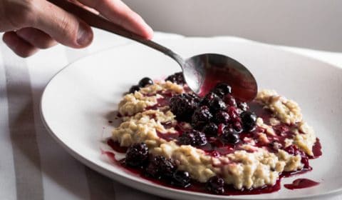 A photo of stewed berries being spooned over the top of porridge.