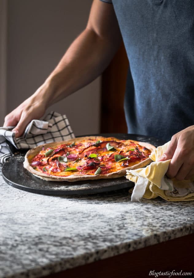 A photo od some holding a pizza slate with Margherita pizza on it.