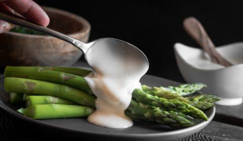 Hollandaise sauce being spooned over a plate of blanched asparagus.