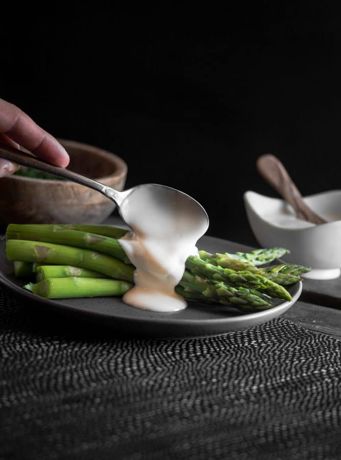 Hollandaise sauce being spooned over a plate of blanched asparagus.