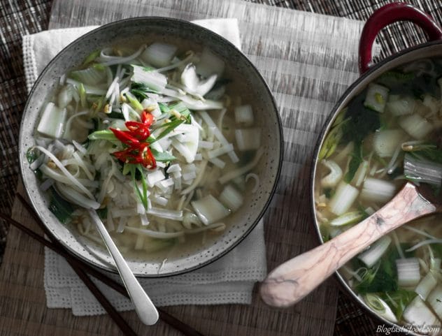 A overhead photo of a chilli noodle broth filled with vegetables. 