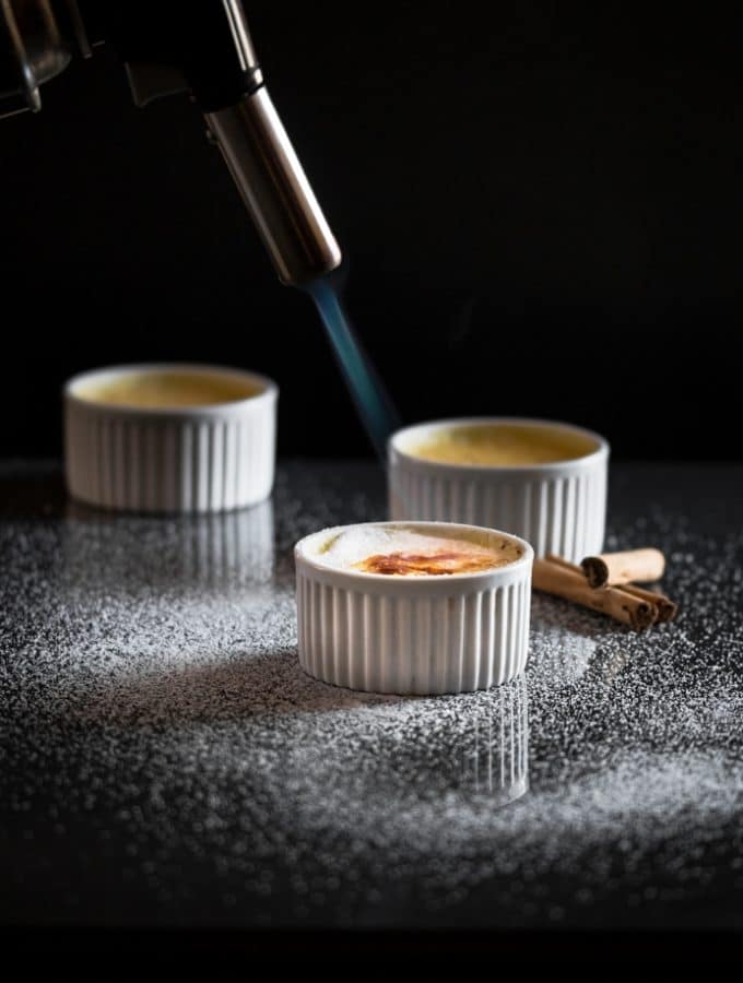 Someone using a blowtorch to caramelise sugar on top of baked custard in a ramekin to make creme brulee.