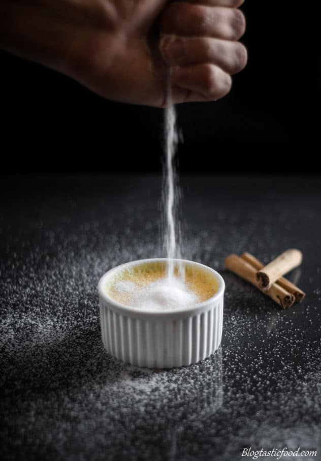 Sugar being sprinkled over a ramekin filled with baked custard. 