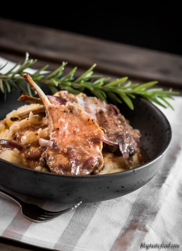 A bowl of medium rare lamb chops and potato puree that has been garnished with a sprig of rosemary, 