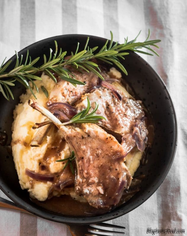 A photo of lamb rack, pureed potatoes and onion gravy in a black bowl. 