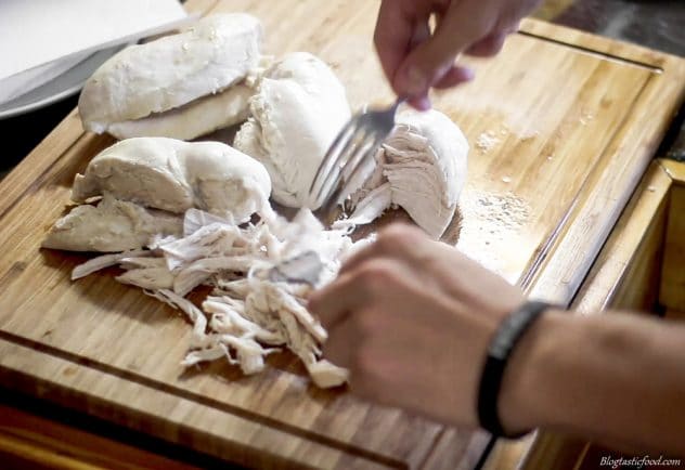 A photo of someone using 2 forks to shed poached chicken breasts.