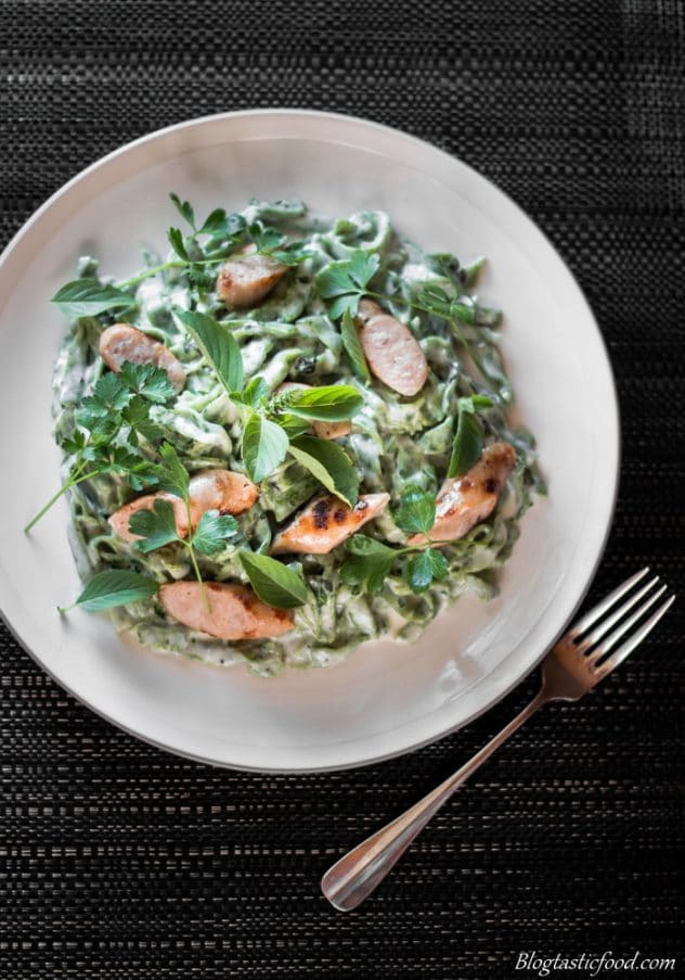 A plate of green pasta with grilled sausages served on a white plate. 