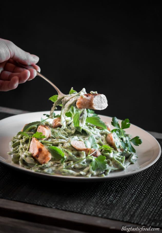 Someone picking some green pasta with sausages with a fork. 