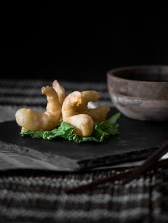 A dark contrast photo of tempura prawns served on a sushi platter, garnished with a bundle of lettuce.