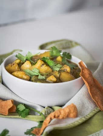 A photo of potato and green bean curry serve in a white bowl.