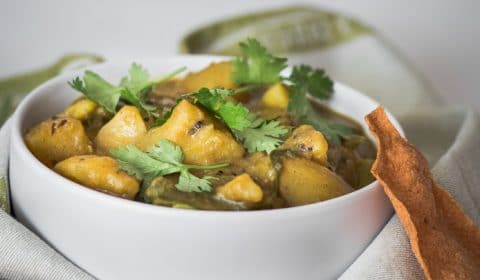 A photo of potato and green bean curry serve in a white bowl.