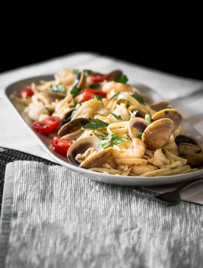 A moody contrast photo of pasta filled with clams, prawns and fish.