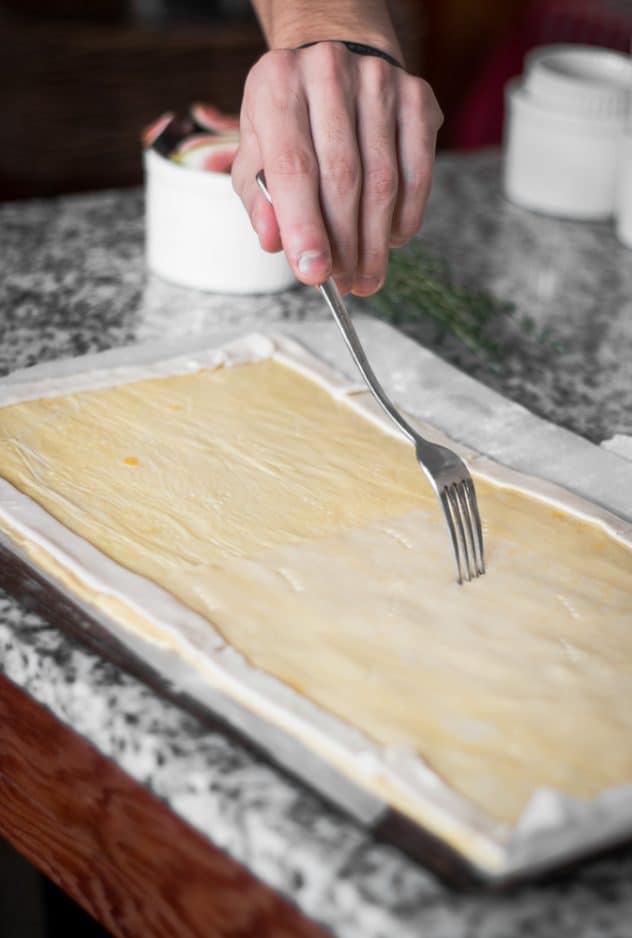 A fork pricking holes into a sheet of puff pastry.