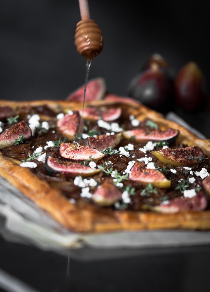 A photo of a fig and onion tart with honey being drizzled over the top.