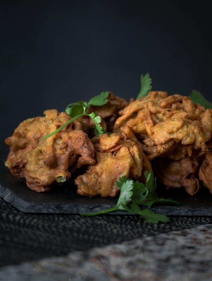 A photo of golden onion bhajis and coriander served on a platter.